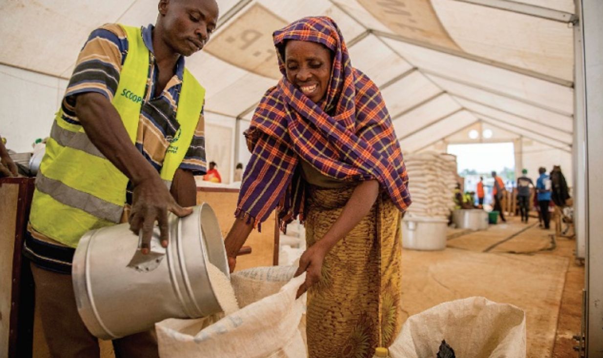 Grain being measured into a sack at a distribution site, from Quad Tee's food security in Uganda article