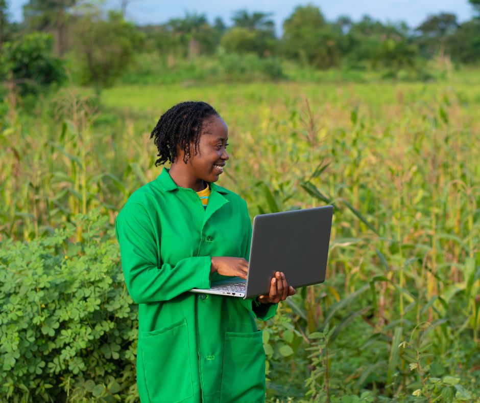 Woman agripreneur using a laptop in a crop field, representing digital and agriculture finance for women